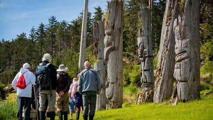 Group of people look at several totem poles. 