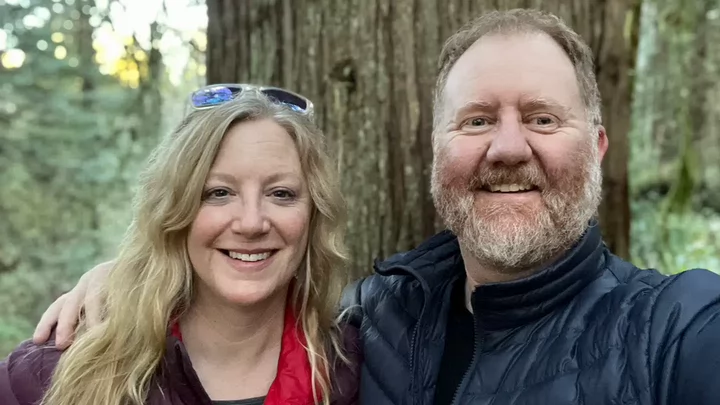 Woman with shoulder length hair standing beside a man with a beard and smiling. 