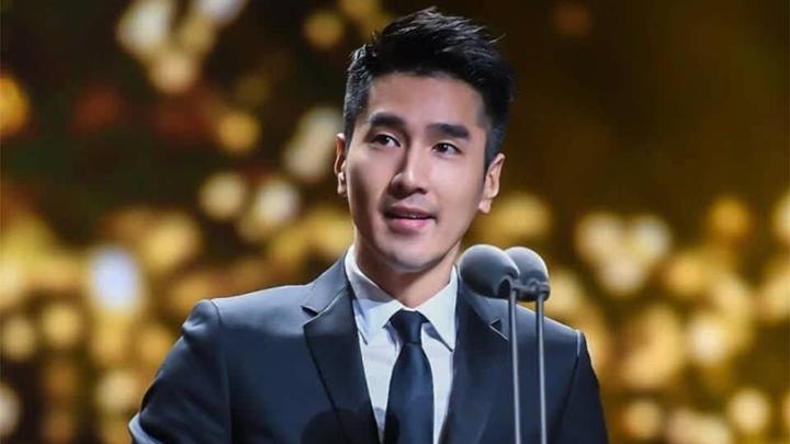 Man in a suit speaking in front of microphone.