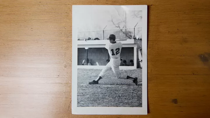 A black and white photo on a wood background of a uniformed baseball player taking a swing at the ball. 