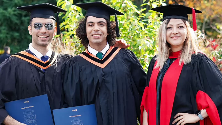Three students in graduation gowns and hats standing side by side and smiling.