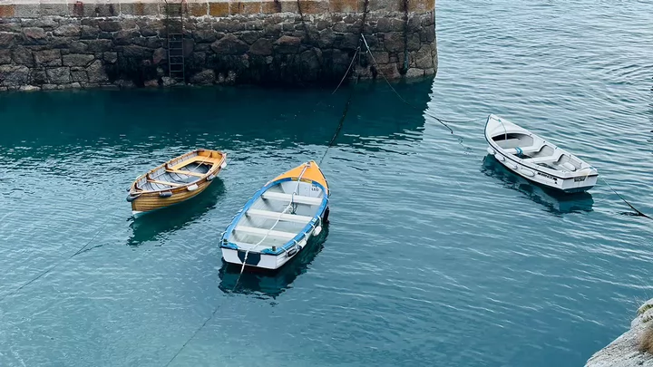 Three wooden row boats floating in a harbour.