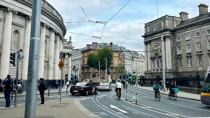 A busy street filled with cars, bikes and pedestrians outside of Trinity College in Dublin, Ireland.