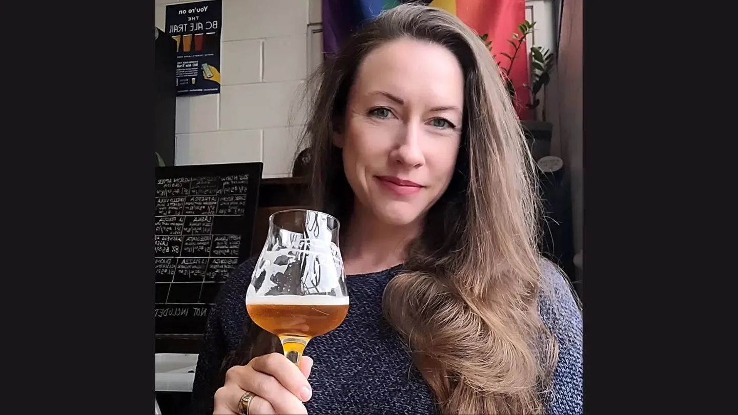 A woman with long hair holding up a glass filled with beer. 