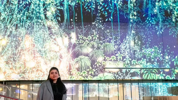 A woman standing in front of a digital image of a tree on a digital billboard in New York City's Times Square.