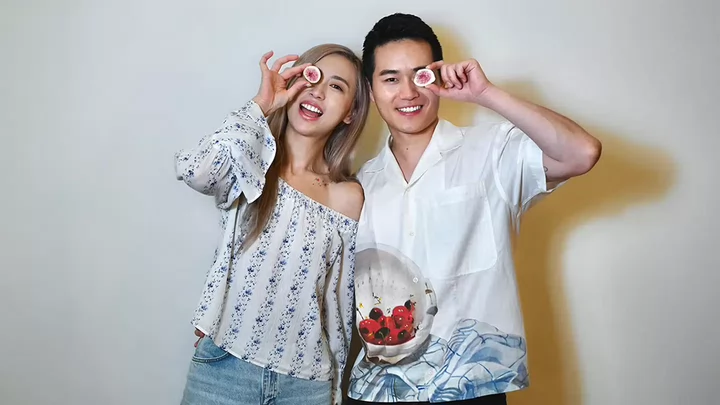 Two people smiling and holding a half-cut fig in front of their eyes.