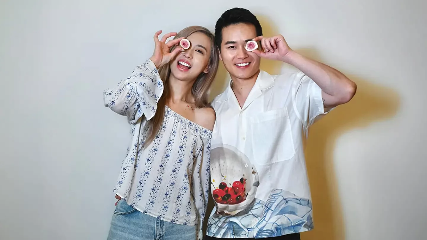 Two people smiling and holding a half-cut fig in front of their eyes.