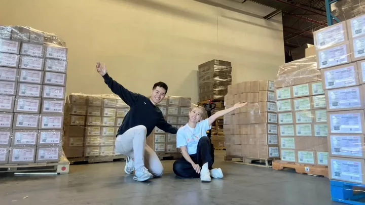 Two people smiling and pointing to stacks of boxes in a warehouse. 