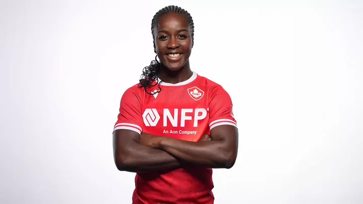 A woman's rugby player in her team uniform crossing her arms and smiling.