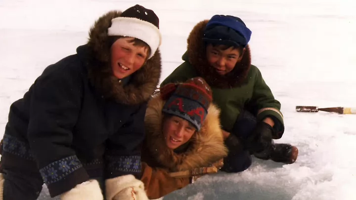 An old photo of three children wearing winter gear in the snow.