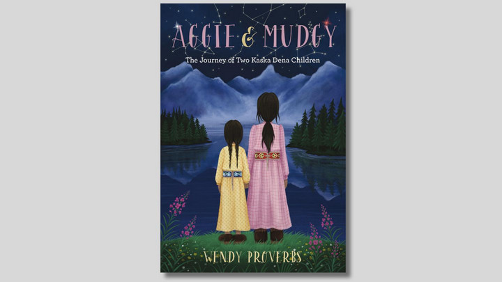 Cover of a book titled Aggie & Mudgy: The Journey of Tow Kaska Dena Children by Wendy Proverbs, featuring a drawing of two long-haired girls holding hands and looking at a lake and mountains.