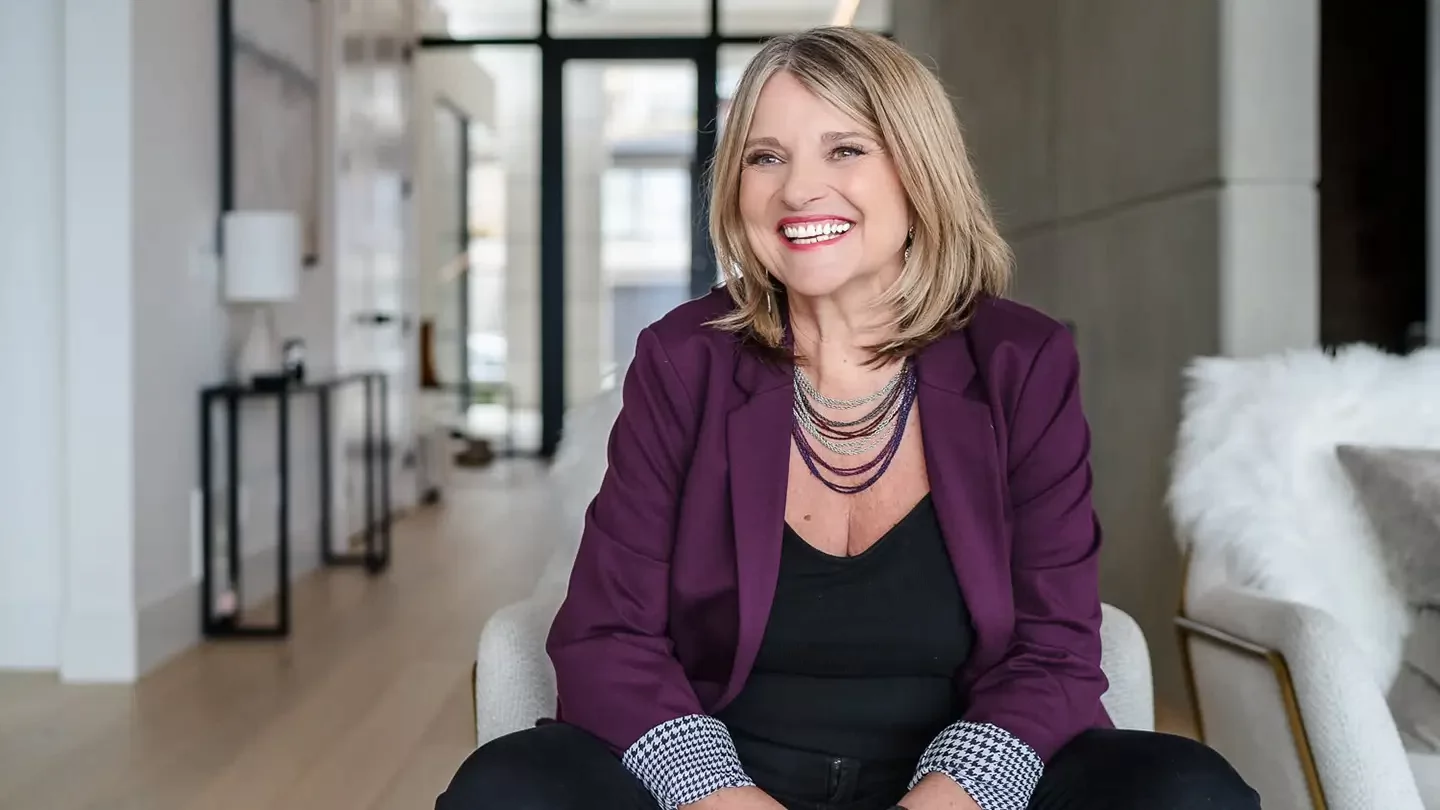 Woman with shoulder length hair sitting on a chair in a stylish and airy apartment suite smiling. 
