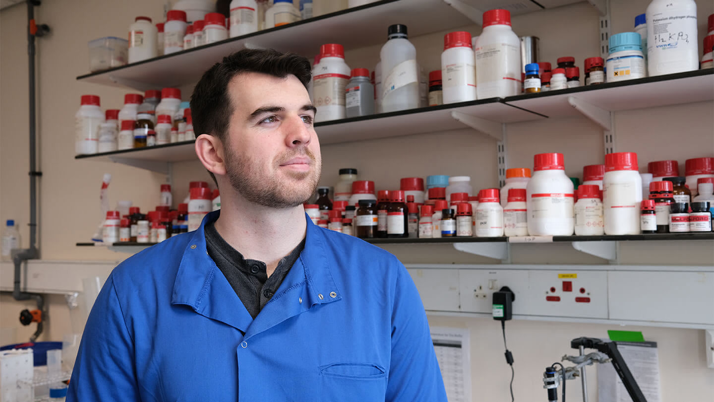 Man in a blue shirt standing in front of three shelves filled with medicine bottles.