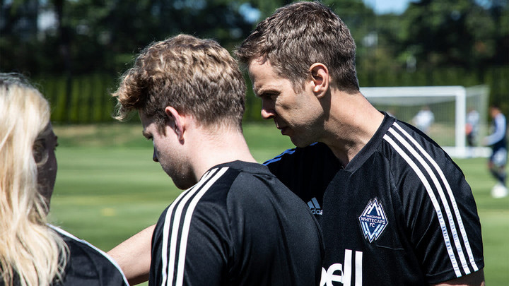 Man instructing younger man and woman on soccer field. 