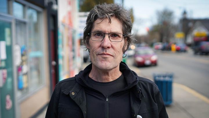 Man wearing glasses standing on the sidewalk. 