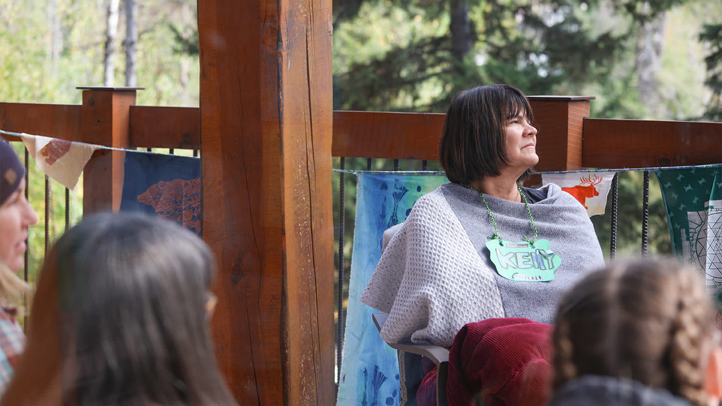 Woman sitting in a group on a porch wearing a shawl and a lanyard with a nametag that says Kelly.