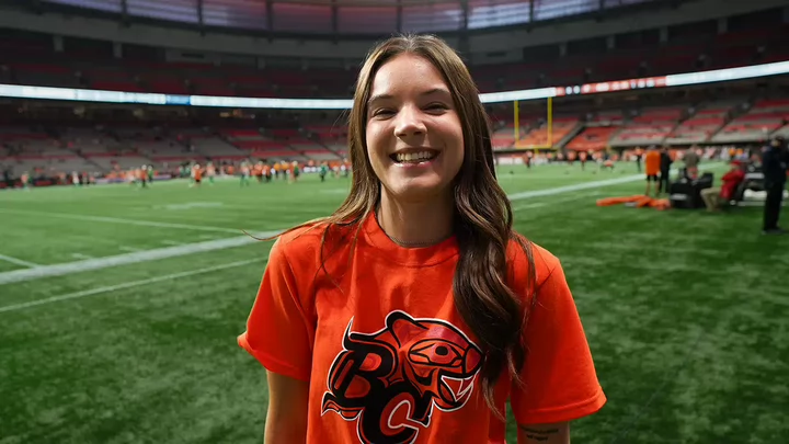BC Lions employee Trinity Stanger smiling on the sidelines of a BC Lions game at BC Place stadium.