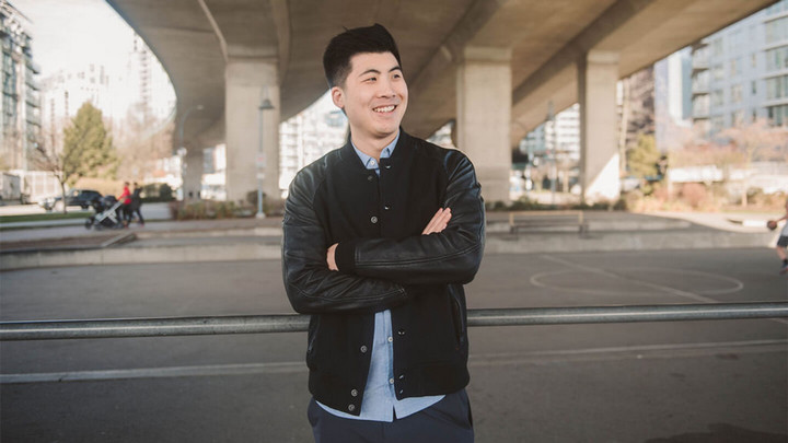 Man standing arms crossed and smiling outside under a viaduct.