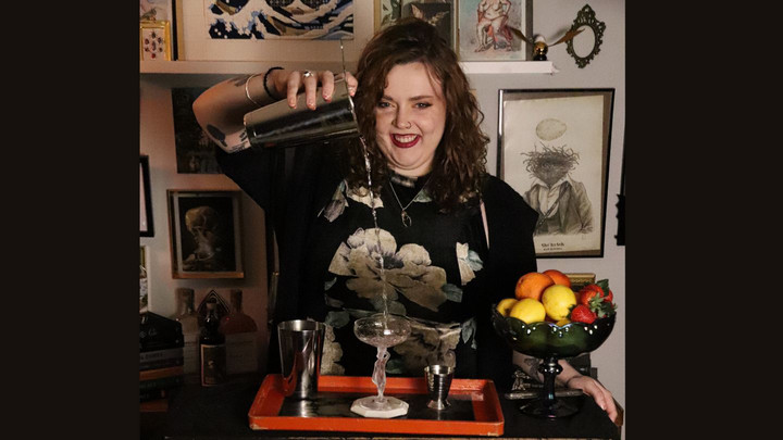 Person pouring liquid from a cocktail mixing container into a coup cocktail glass. 