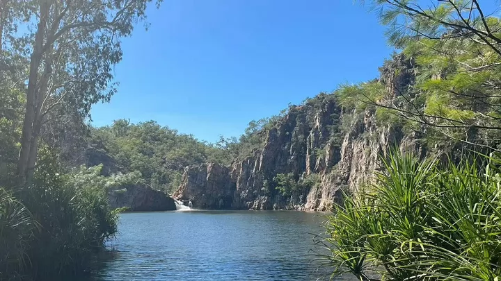 Water flowing over rocks into a larger body of water surrounded by green tropical foliage.