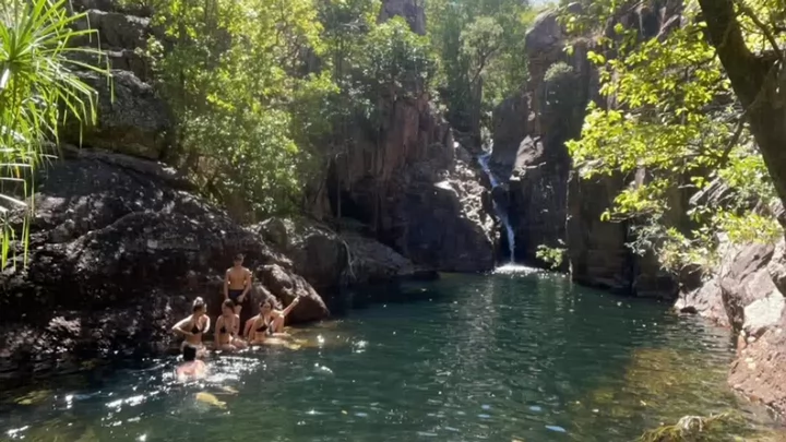 People swimming near a small waterfall. 