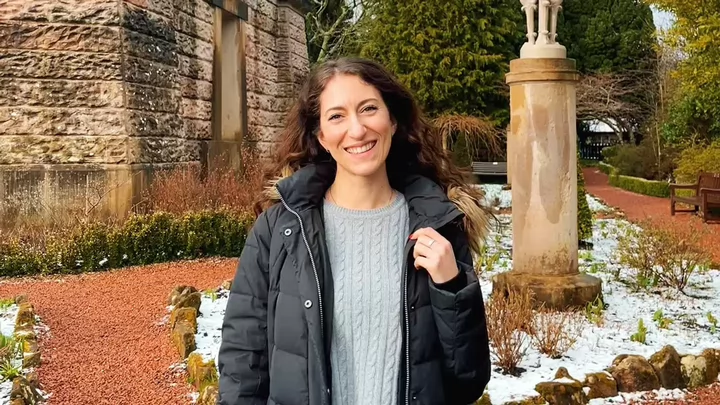 Woman wearing a parka and smiling outside of a castle.