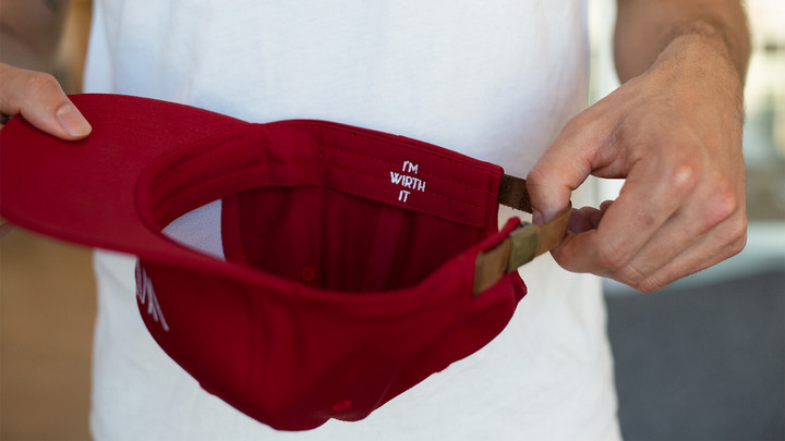 An upside-down red baseball cap being held by a person with a white shirt.