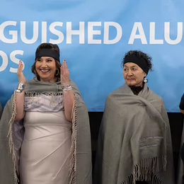 Women raising her hands beside another woman during Indigenous blanketing ceremony.