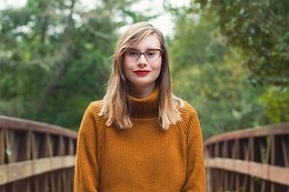 Woman with thick glasses and a sweater standing outside. 