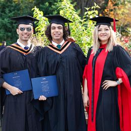 Three students wearing graduation caps and gowns standing outside.