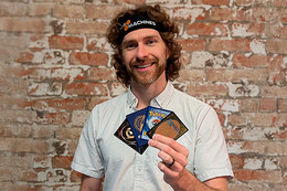 Man holding up trading cards and wearing headband that says TCG Machines