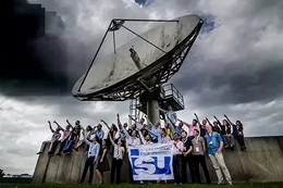 People pointing at the sky while standing beneath a large satellite dish.