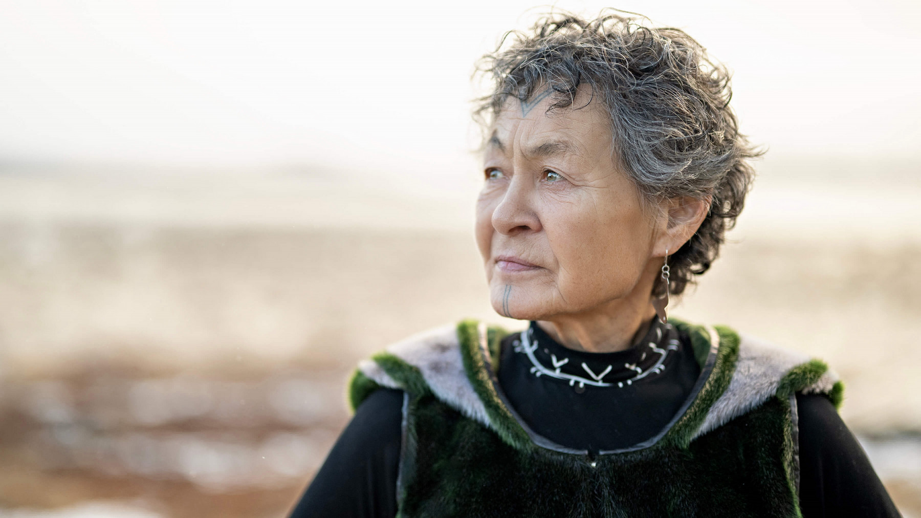 Woman with Inuit tattoos on her face wearing fur tunic looking into the distance.