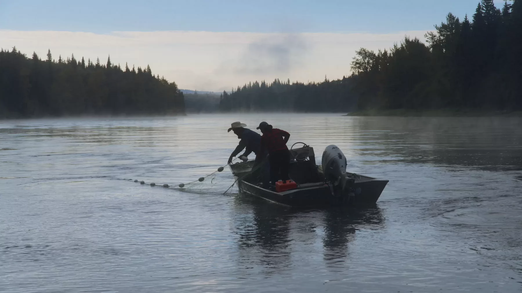 Two people in an aluminum boat floating on a river haul in fishing nets.
