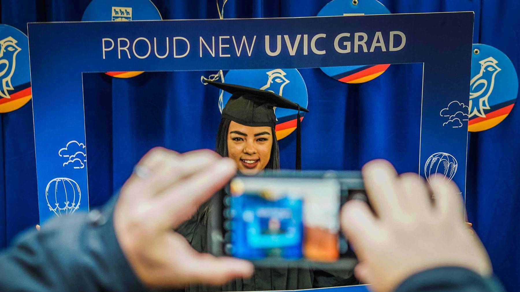 New grad posing for a photo within a blue square cardboard frame