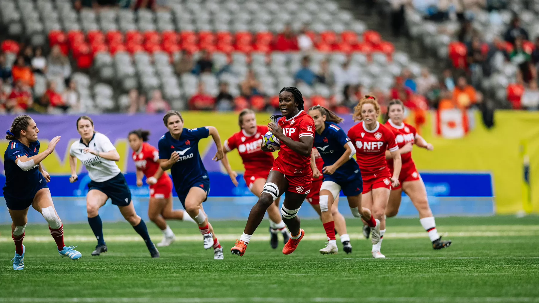 A woman wearing a Team Canada Rugby uniform runs downfield with a rugby ball past her opponents. 