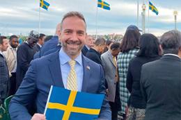Man in blue suit at public event holding a Swedish flag. 
