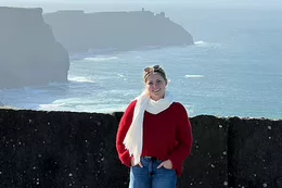 UVic grad Nina Simons stands against a wall overlooking the coast of Ireland.