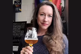 A woman with long hair holding a glass of beer. 