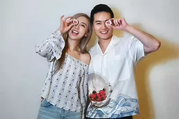 Two people smiling and holding a half-cut fig in front of their eyes.