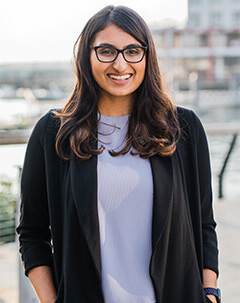 Woman with long hair and classes standing outdoors smiling. 