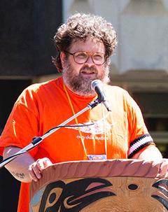 Man in orange shirt standing at a podium.
