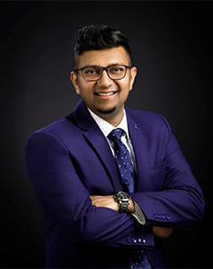 Man wearing suit and tie and glasses standing arms crossed and smiling. 