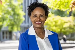A woman wearing a blue blazer and white shirt smiling on a university campus.