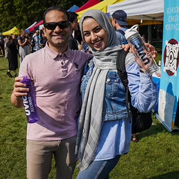 Two people standing at an outdoor event holding water bottles that read UVic Alumni and smiling. 