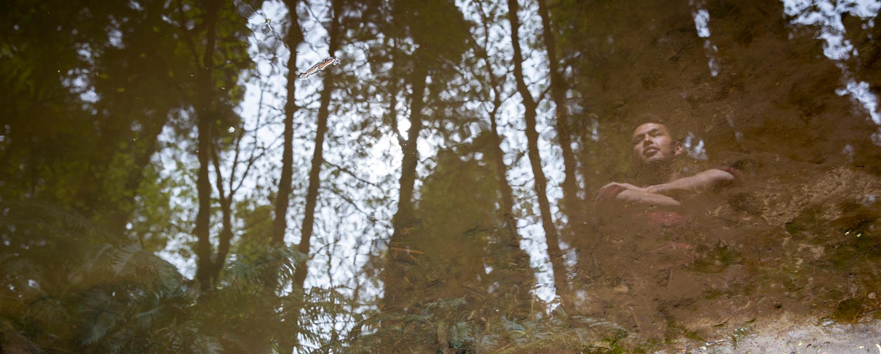 Indigenous person reflected in pool of water in forest