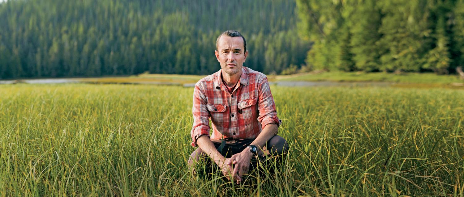 Chris Darimont crouches down in a green field of grass