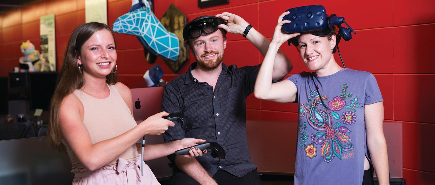 three students pose with virtual reality goggles