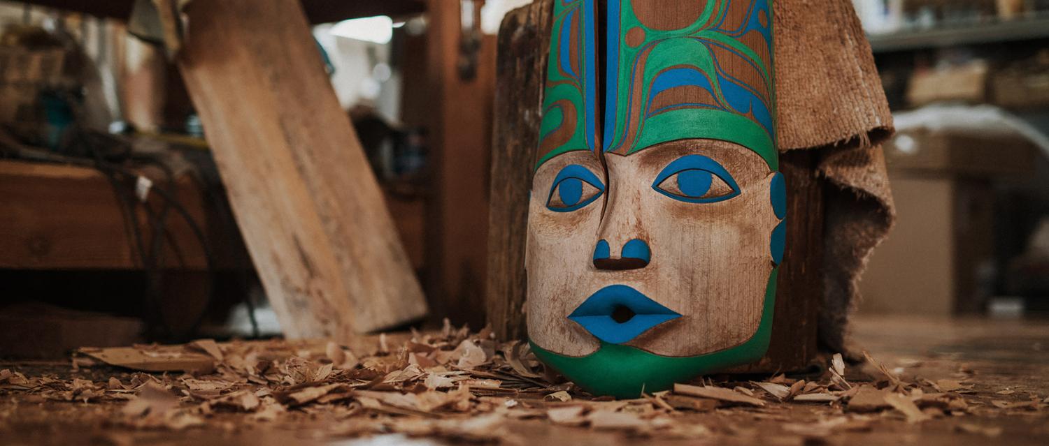 Stunning indigenous carving of a face that sits on the ground with wood shavings all around the ground.