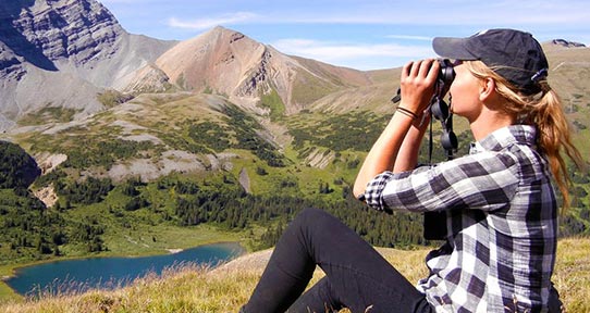 Student on a mountainside looking through binoculars